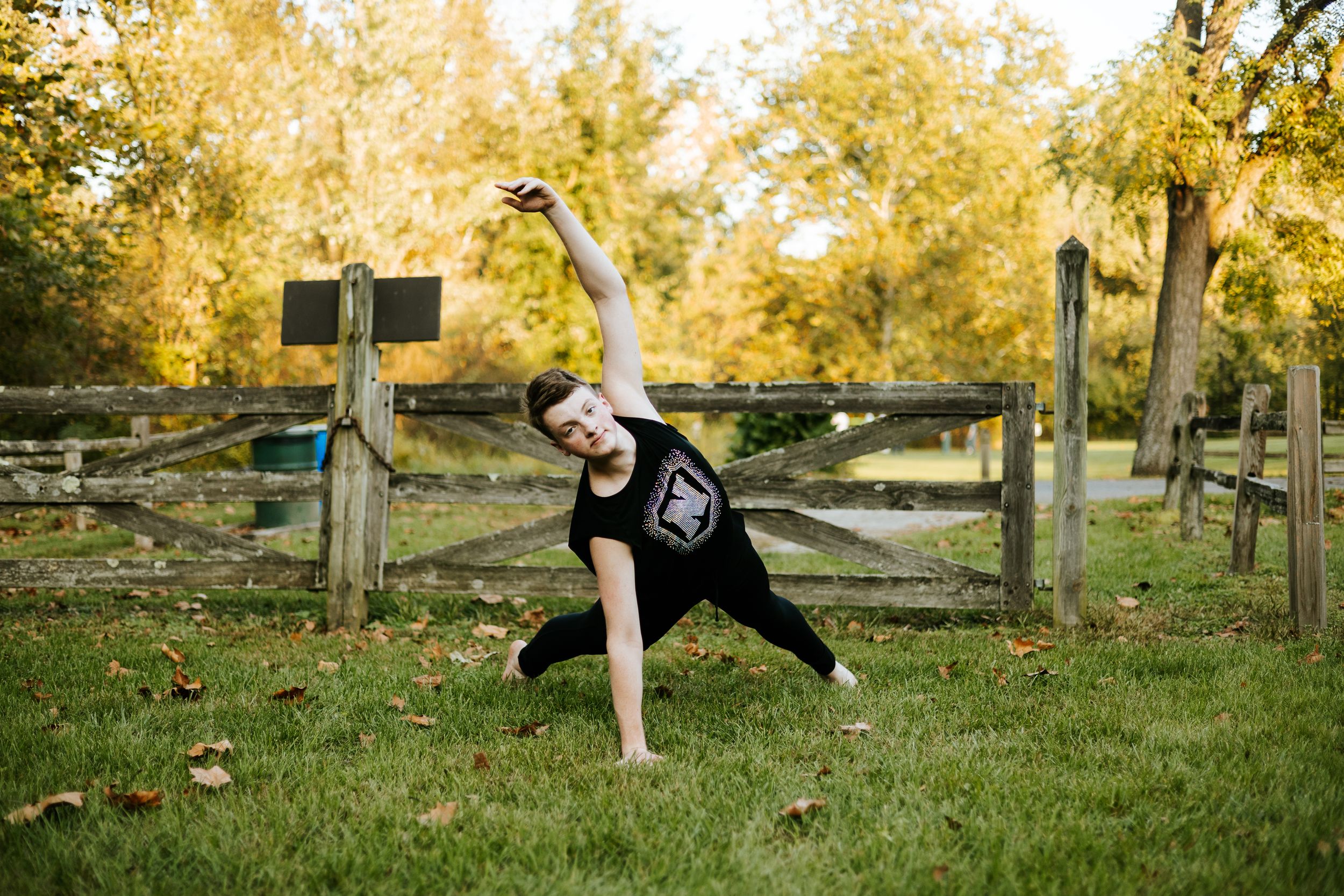 Person jumping and playing in a park with autumn trees and fallen leaves in the background.