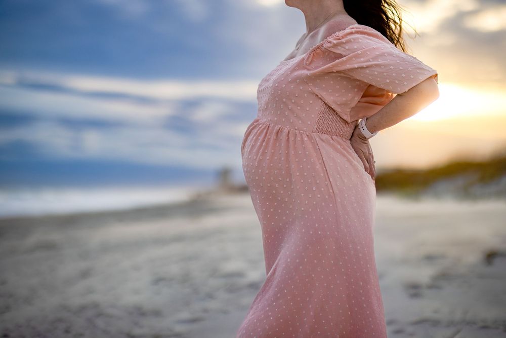 Expectant mother in a pink dress on the beach during a destination maternity session in Orange Beach, Alabama