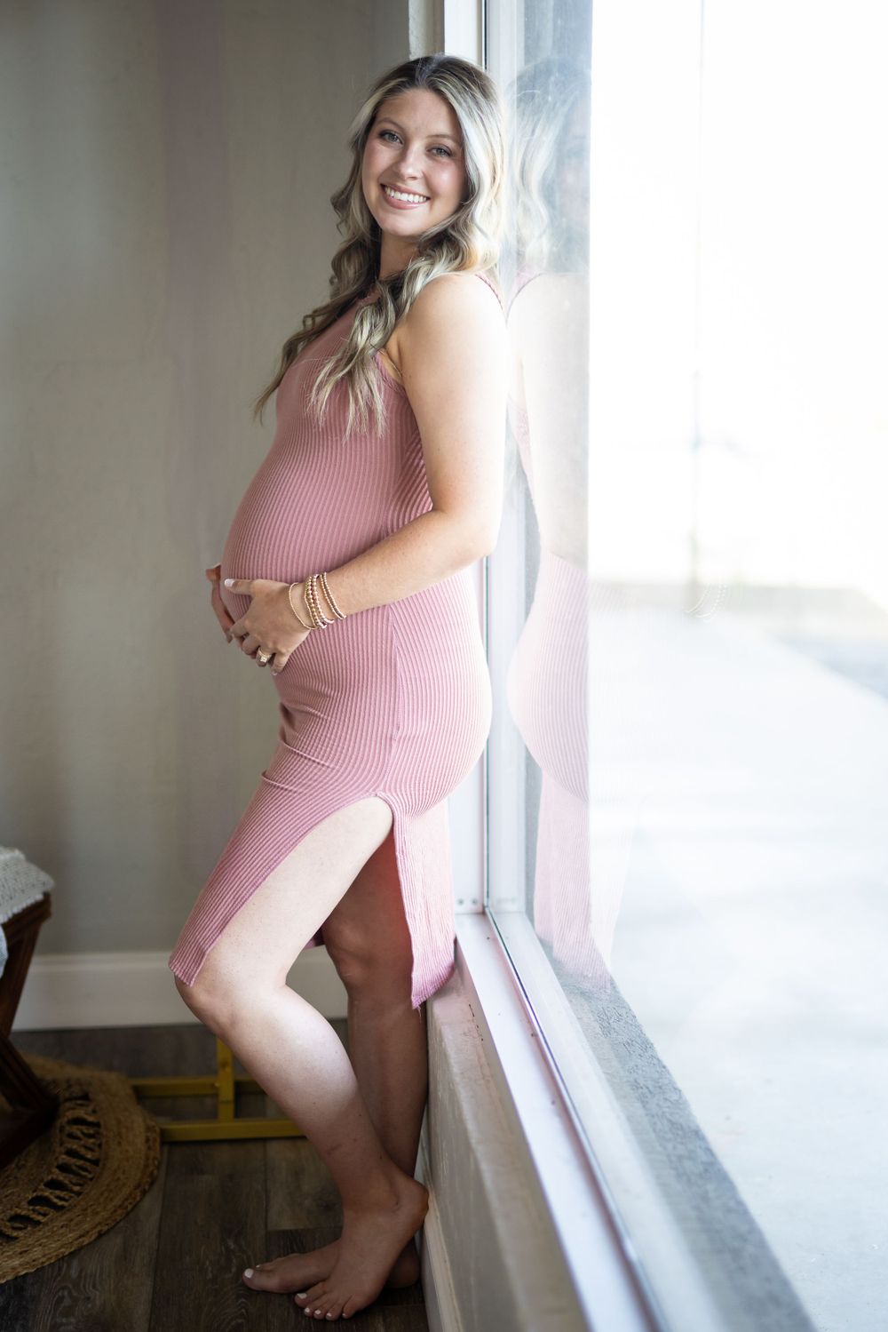 Expectant mother in a pink dress by a window during a studio maternity session in Mountain Home, Arkansas