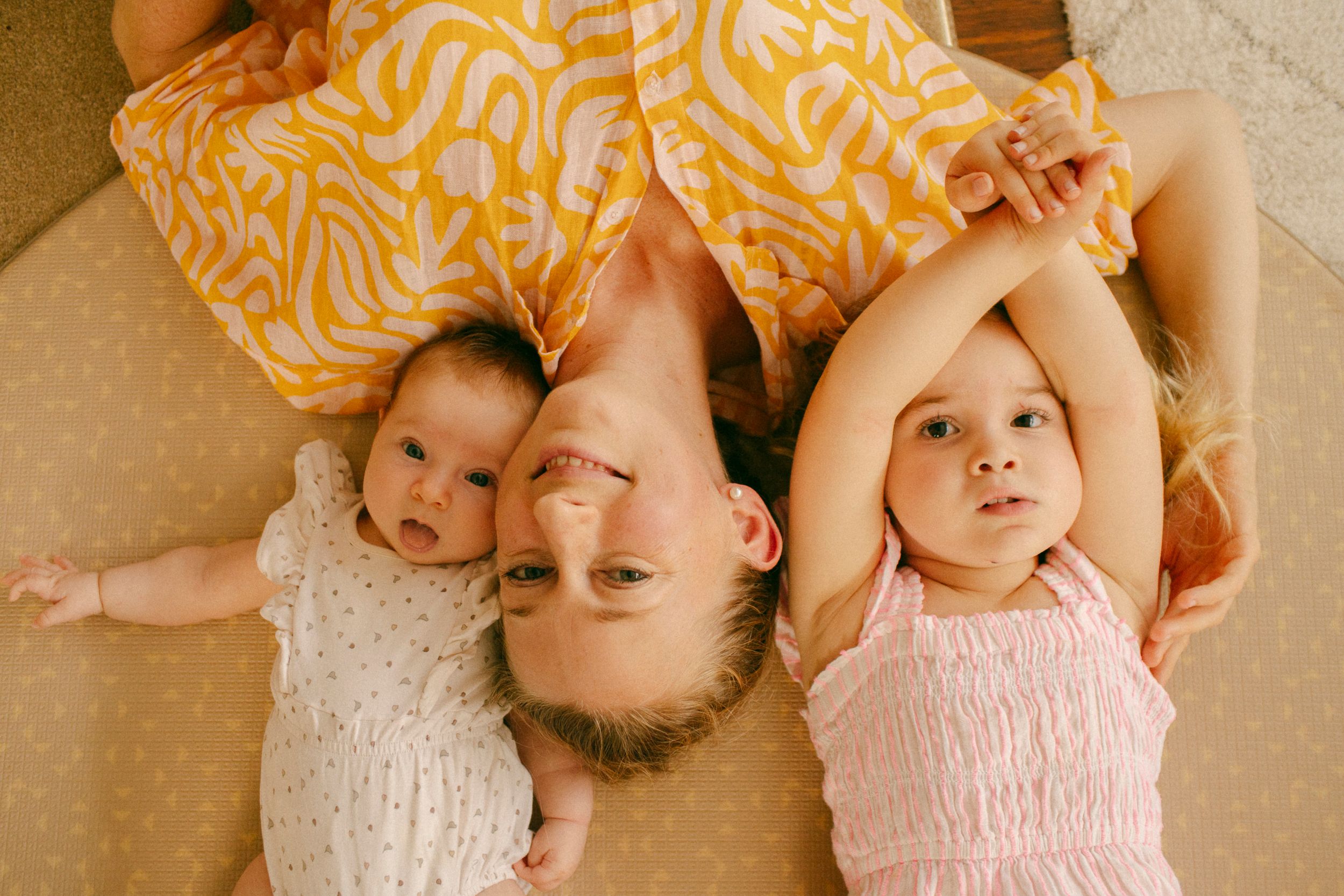 Overhead family photography of a mother and her two daughters looking at the camera in Sydney & Northern Beaches, capturing joyful and intim