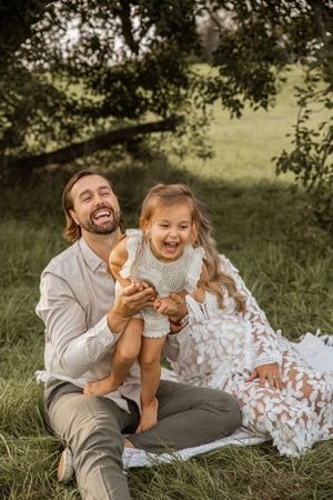 A joyful moment shared under a tree on a picnic blanket, with playful laughter in the warm afternoon sun.