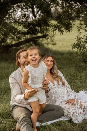 A joyful family shares a candid moment together while relaxing on a blanket in a sun-dappled meadow.