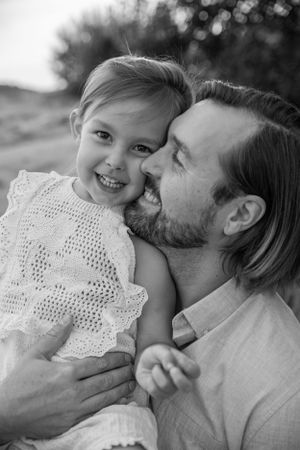 A tender black and white portrait of a parent and child in lace dress sharing an affectionate moment outdoors.