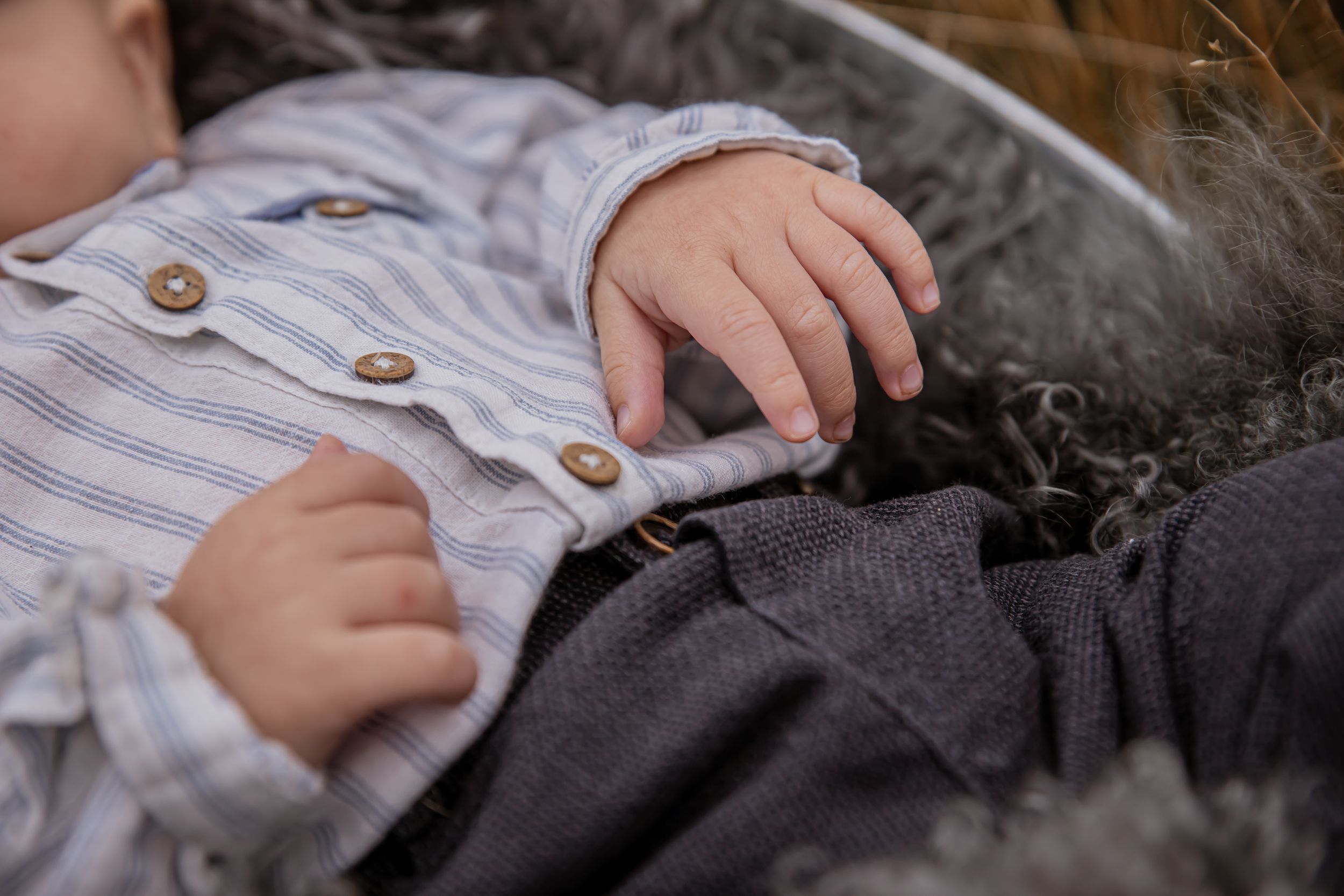 Close up of small hands wearing striped shirt while resting on soft gray fabric.