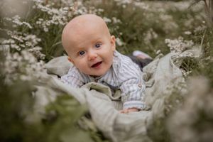 Happy baby in striped onesie lays among white wildflowers in a dreamy outdoor setting.