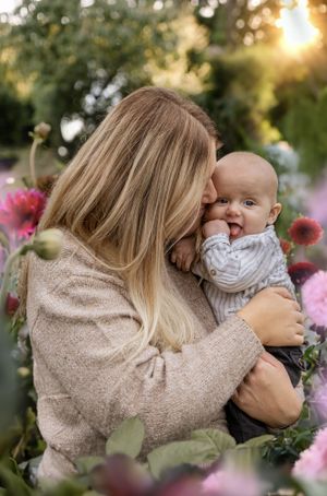 A tender moment between mother and baby surrounded by pink flowers at sunset in a garden.