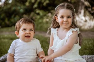 Children sharing a sweet moment together while sitting outside in summer clothing.