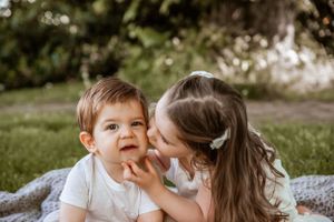 Two children share a sweet moment together while sitting on a blanket in a sunny garden setting.