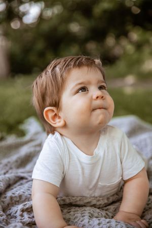 Young child in white t-shirt lying on blanket outdoors looking up with curiosity while enjoying nature.