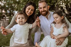 A family in white clothing sits together on grass during a warm summer day outdoors.