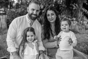 A black and white portrait of a family of four sitting together outdoors.