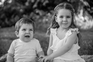 Black and white portrait of two children sitting together outdoors on a blanket with natural lighting.