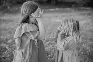 Two young girls in flowing dresses playing together in a meadow, captured in black and white.