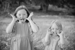 Two children in matching dresses make silly faces while standing outdoors in a black and white photograph.