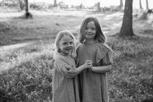 Two figures in matching dresses share a sweet embrace while laughing together outdoors in black and white.