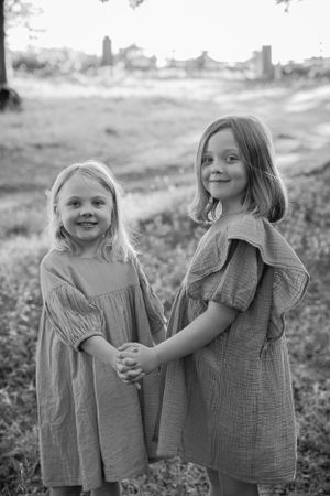 Two children in matching linen dresses hold hands while standing in a field with a misty background.