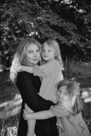 A black and white portrait of a family embracing each other outdoors with trees in the background.