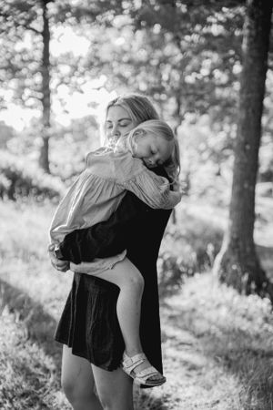 Black and white photo showing tender embrace between parent and child in a sunlit forest setting.