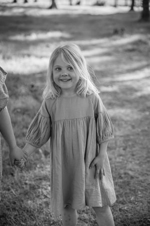 A young child in a light-colored dress with puffy sleeves stands outdoors in a black and white photograph.
