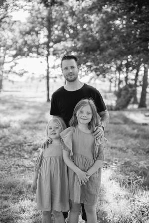 A black and white outdoor portrait of a family group standing together in a wooded setting.