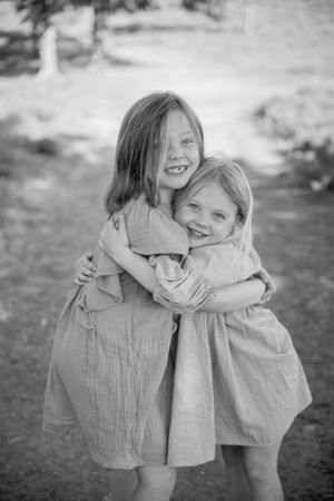 A heartwarming black and white photo of two young children hugging and laughing together outdoors.