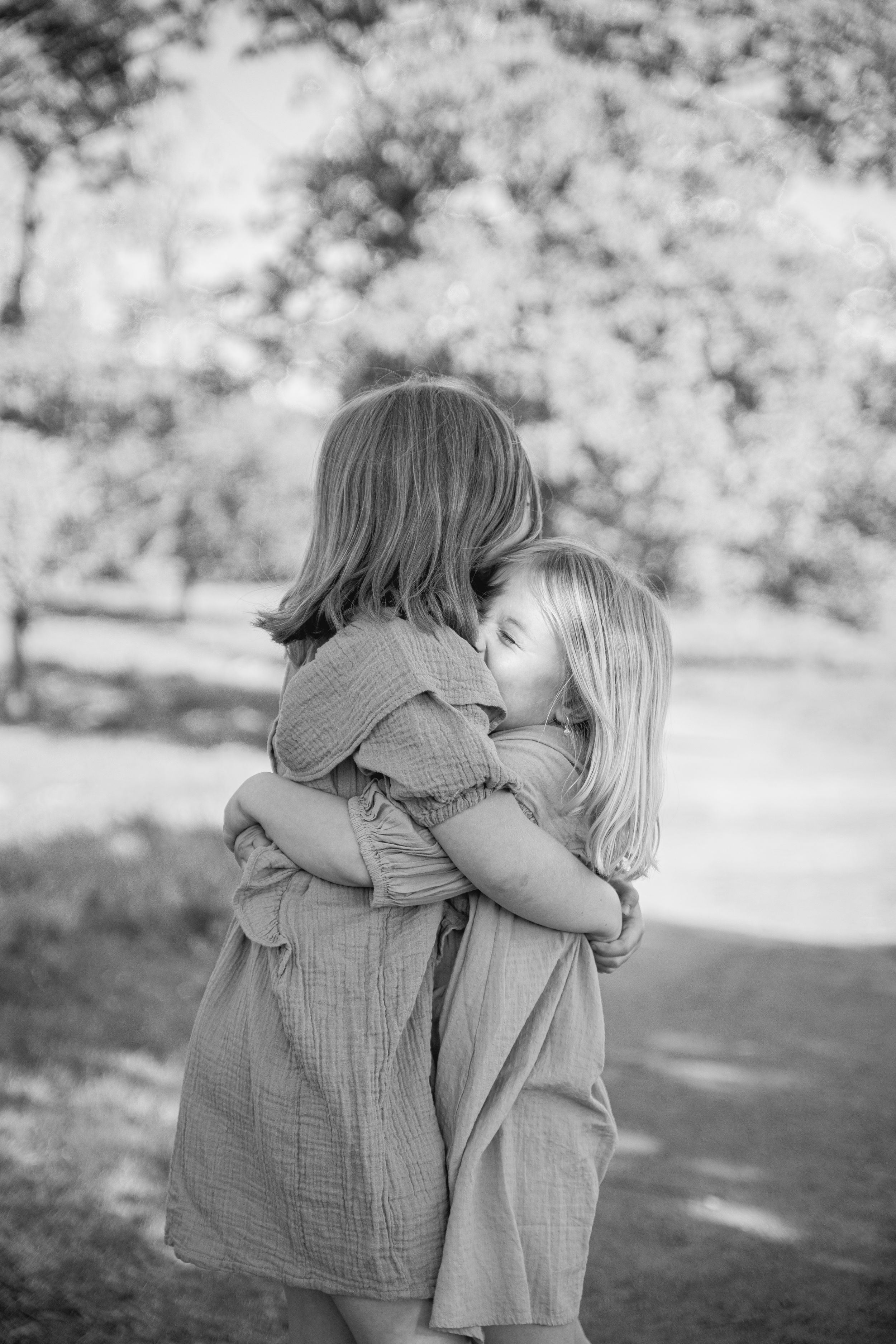 Two children embrace in matching dresses during an outdoor black and white portrait session.