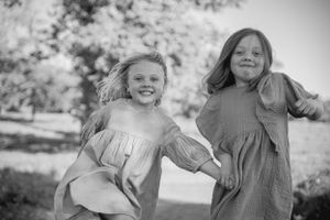 Two children in casual dresses run and play together outdoors in a black and white photograph.