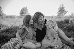 Black and white candid photo of three people sharing an intimate moment while sitting on a blanket outdoors.