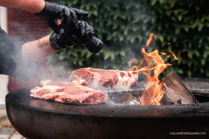 Close-up of meat grilling with flames and smoke on an outdoor barbecue.