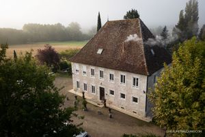A historic white manor house with traditional architecture surrounded by countryside.