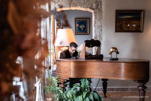 A vintage wooden piano sits in an elegant room with framed artwork and a table lamp.