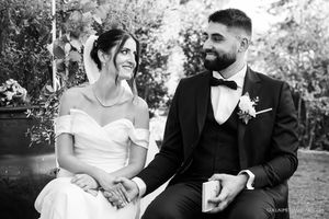 A black and white portrait of a couple seated outdoors at their wedding.