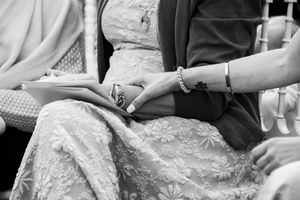 Close-up detail of hands resting on a lace dress during a wedding ceremony.