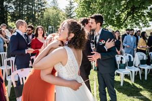 Wedding guests celebrate outdoors under trees during a summer ceremony.