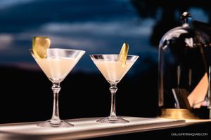 Two martini glasses with garnish on a bar counter at dusk.