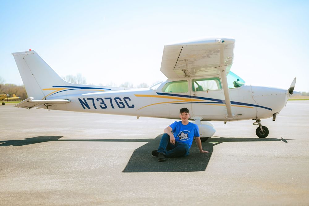 A series of light aircraft parked in a row on an airport tarmac under bright sunny skies.