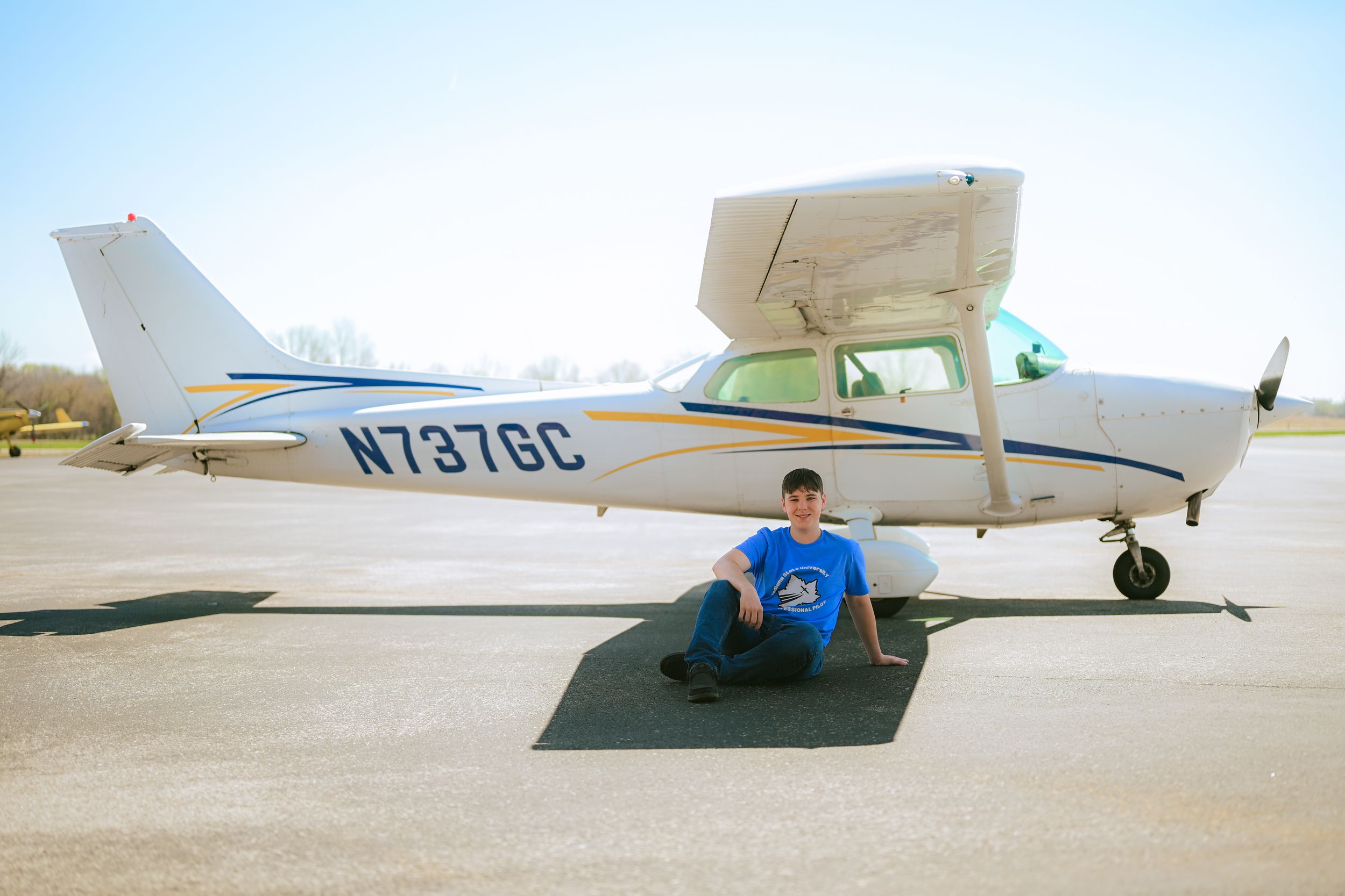 A series of light aircraft parked in a row on an airport tarmac under bright sunny skies.