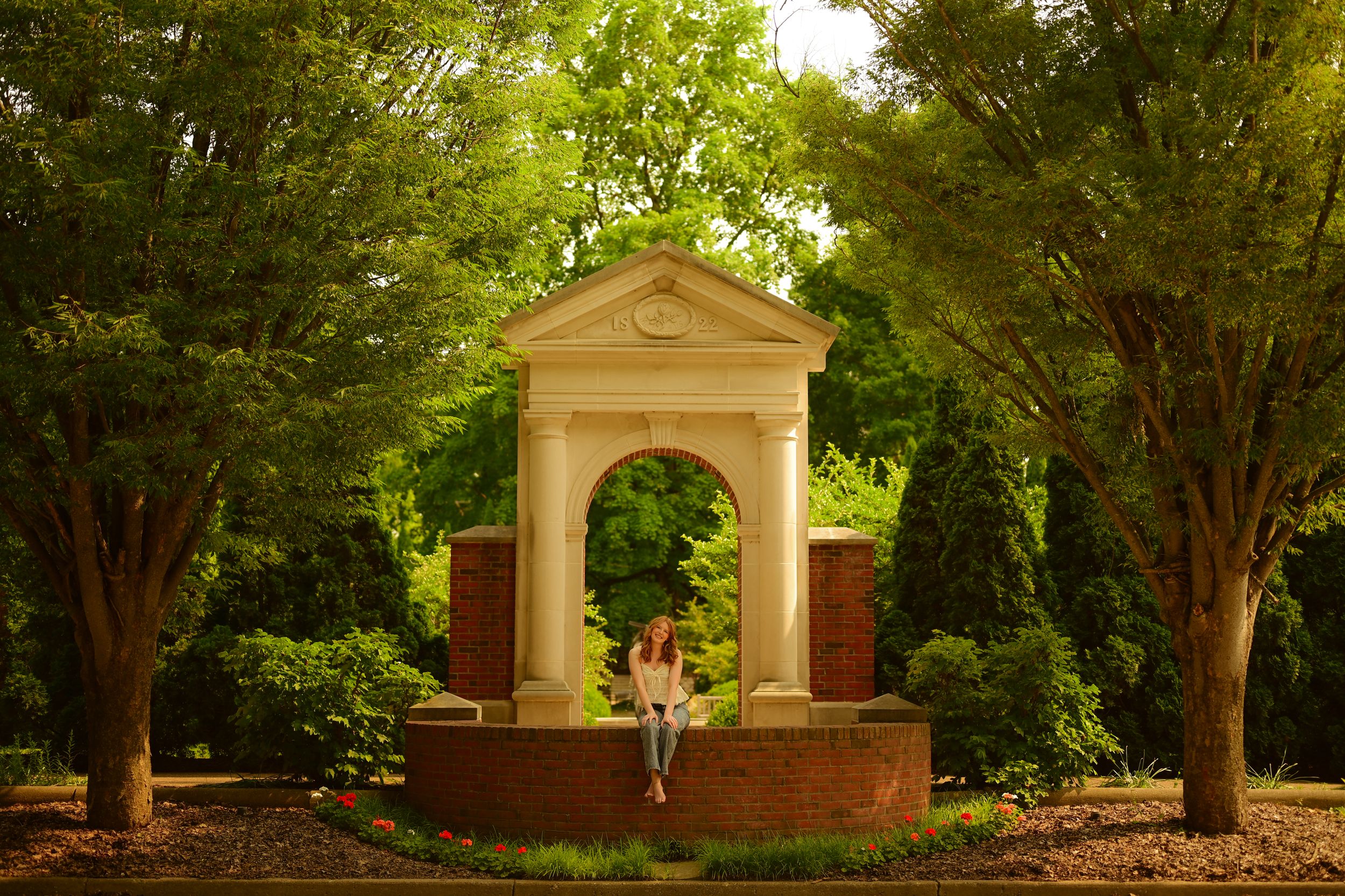 Historic brick archways and gateway structure along a tree-lined path in a formal garden setting.