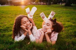 Two friends lying on grass in matching socks enjoying a sunny afternoon together in the park.
