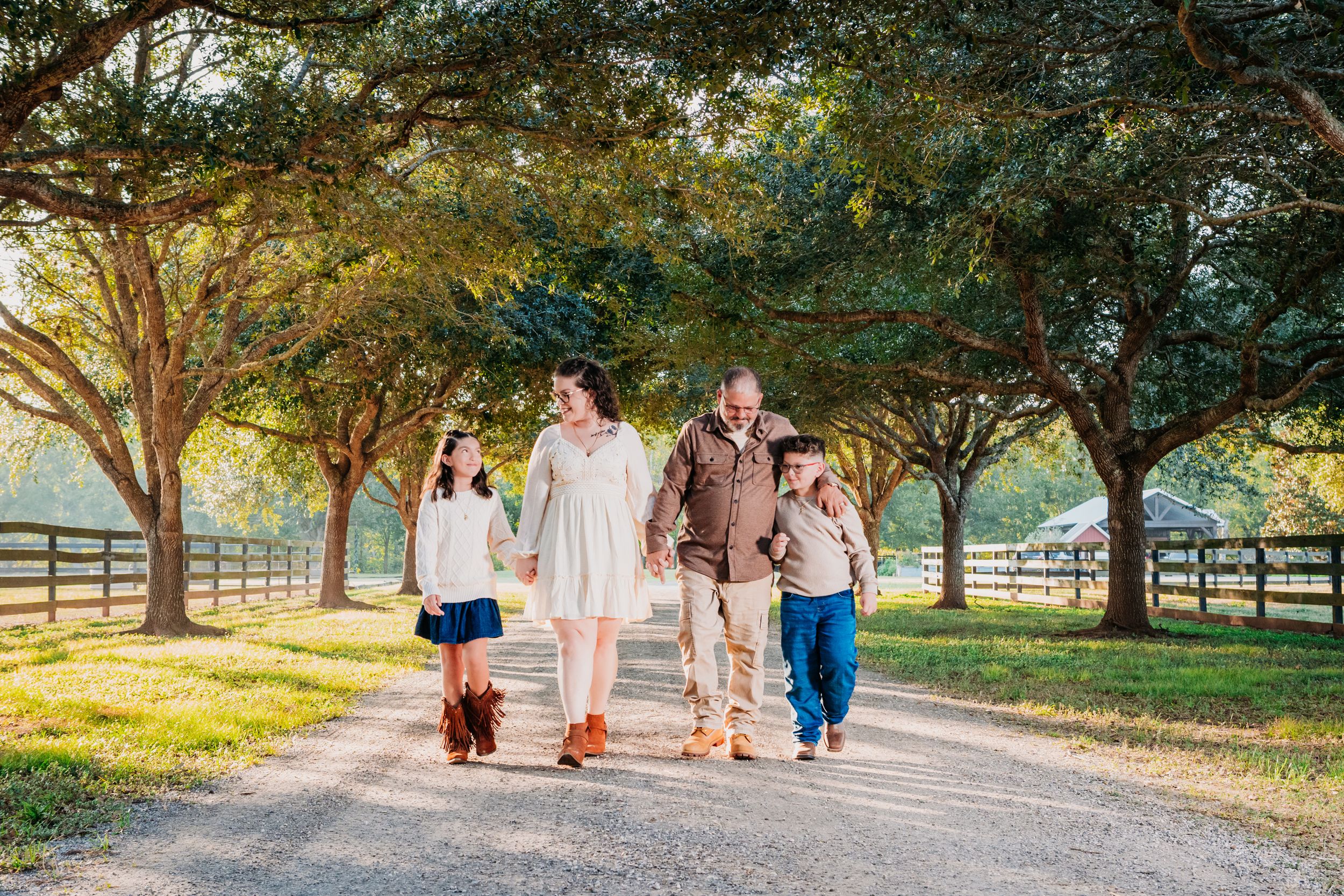 Family members walk together on a tree-lined path during a sunny afternoon photo session. Country