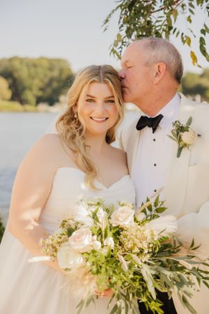 A tender outdoor wedding portrait by a lake with a white floral bouquet.
