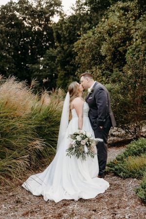 A couple shares a romantic kiss among tall ornamental grasses in a garden setting.