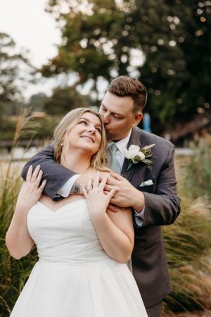 A joyful wedding embrace captured in a natural outdoor setting with ornamental grasses.