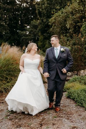 Couple walking hand in hand on garden path in wedding attire.