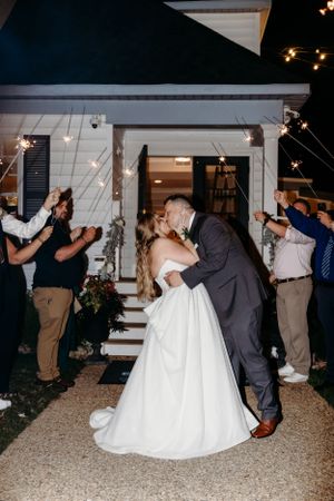 A wedding exit celebration with sparklers as the newlyweds share a kiss on outdoor steps.