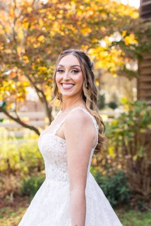 Bride in white lace wedding dress poses against golden fall foliage.
