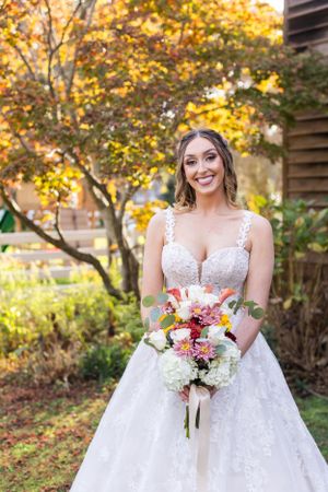 Bride in white lacey gown holds vibrant bouquet during outdoor autumn photo session.