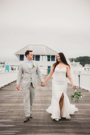 Wedding couple walking hand in hand on wooden pier by coastal gazebo.