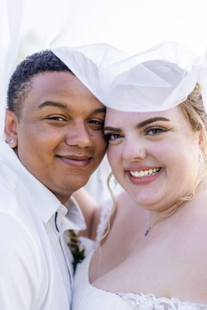 A loving couple shares intimate moments in white attire against a bright background.