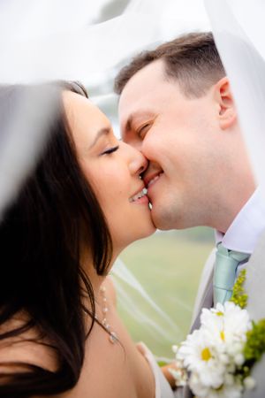 Intimate wedding photo showing a romantic kiss through a delicate veil with white flowers in the foreground.